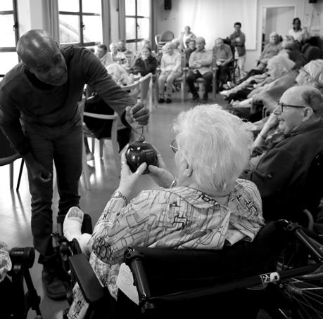 Jean-Marc accompagne une résidente tenant un instrument à l’Hôtel-Dieu, en noir et blanc.