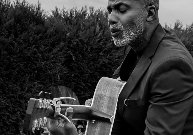 Jean-Marc chante en jouant de la guitare à l’extérieur, en noir et blanc.