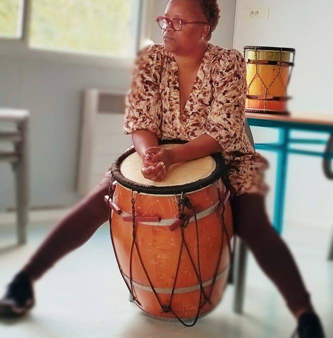 MariCé assise sur un tambour, les mains posées sur l’instrument.
